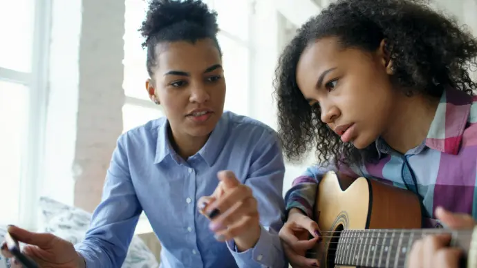 Two young women learning to play guitar together.